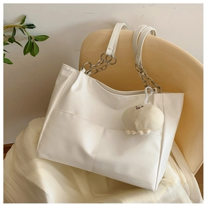 Detail of white leather tote bag featuring geometric stitching and a cute plush pendant