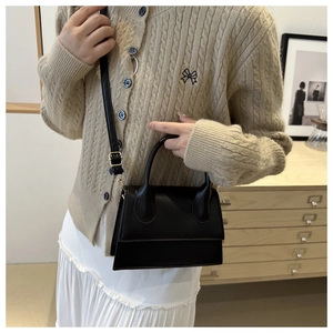 Detail of a black matte leather handbag featuring golden hardware and detachable strap