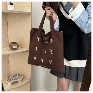 Detail of dark brown corduroy tote bag with white embroidery and dual carry handles