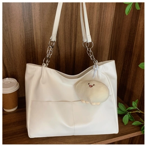 Detail of cream white tote bag with metal chain strap and white plush doll charm