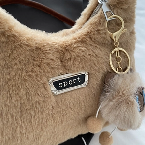 Sac à main tendance en peluche camel avec chaîne dorée et étiquette sport sur fond blanc