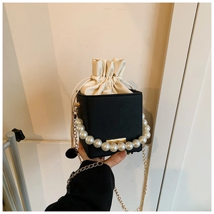 Close-up of black cube crossbody bag with pearl handle and golden chain strap