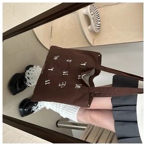 Brown corduroy tote bag with white letter embroidery shown in a vintage mirror reflection