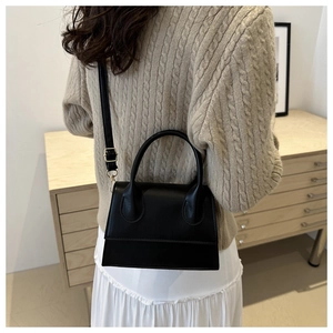 Detail of a chic black leather handbag with gold metal hardware on a beige sweater