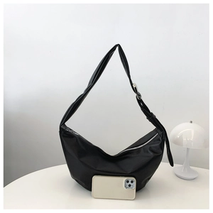 Detail of a black crescent hobo bag in matte leather next to a phone for size scale