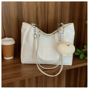 Detail of white leather tote bag with V-pocket and plush smiley charm on a wooden shelf