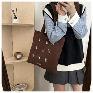 Detail of coffee brown corduroy tote bag featuring white letter embroidery and striped texture