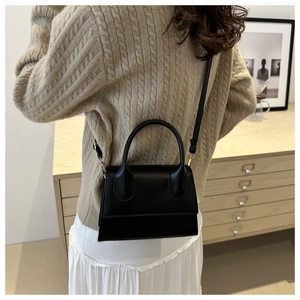 Detail of black mini leather handbag showing structured handle and adjustable strap