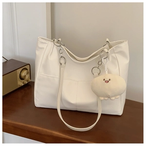 Detail of cream leather tote bag with V-shaped stitching and plush bunny charm accessory