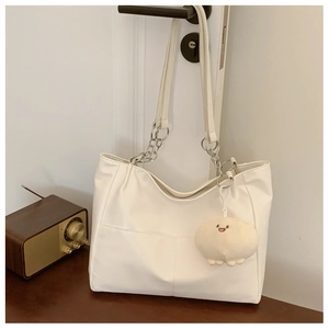 Detailed view of white tote bag featuring metal chains and cute monster plush pendant charm