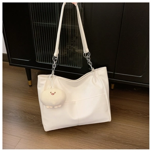 Close-up of white tote bag with silver chain straps and a cute plush keychain charm