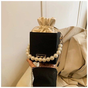 Detail of contrast bucket bag featuring oversized faux pearl handle and gold chain strap