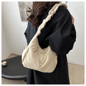 Close-up of off-white pleated cloud bag in lightweight nylon fabric worn over a black coat