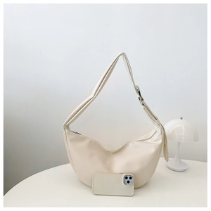 Detail view of cream crescent bag with adjustable strap and smartphone for scale reference