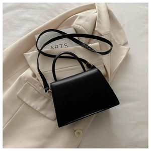 Detail of vintage black trapezoid handbag with gold hardware on a beige blazer