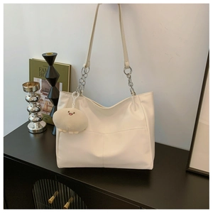 Detail of white tote bag with chain strap and cute plush charm in a home setting