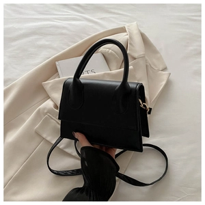Detail of black PU leather handbag with gold hardware and top handle on beige blazer