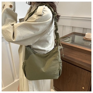 Detail of dark green tote bag with ruffled shoulder strap worn over a beige trench coat