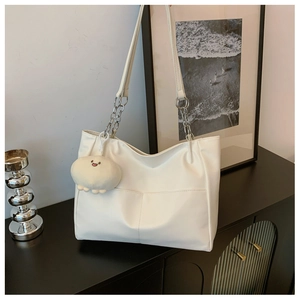 Detailed view of white tote bag with silver chain strap and plush keychain accessory