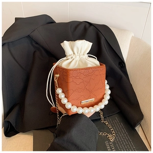 Detail of caramel lace bucket bag with pearl handle and golden chain strap on a chair