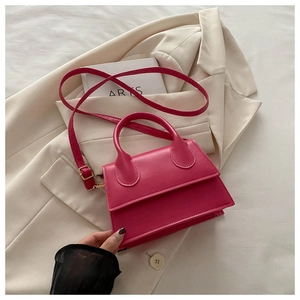 Detail view of a magenta PU leather mini handbag styled on a beige blazer with art books