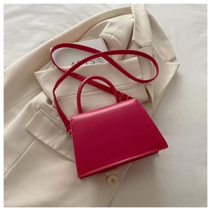 Detail of rose red trapezoidal handbag featuring golden hardware on a beige blazer