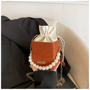 Detail of a brown mini bucket bag with pearl handle and golden chain on a black blazer