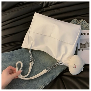 Detailed view of white tote bag with silver chain strap and plush pendant on leather surface