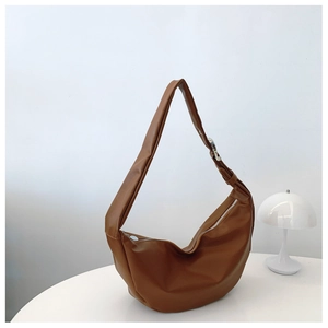 Caramel brown leather crescent bag with adjustable strap on a minimalist white desk