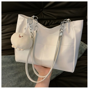 Close-up of white tote bag with metal chain handle and round plush smiley face charm