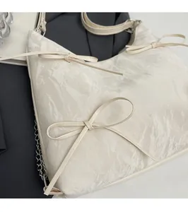 Gros plan d'un sac crème avec nœuds papillon, lettrage fashion et chaîne métallique