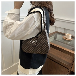 Detail of a brown vintage polka dot shoulder bag with silver bow buckle worn by a model