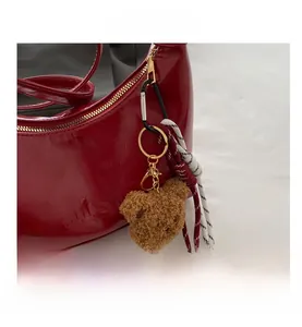 Detail of red patent leather crescent bag with bear charm and woven rope accent
