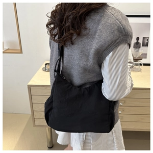 Detail of a minimalist black pleated crossbody bag worn over a gray knitted sweater