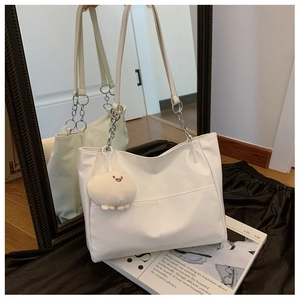 Detail of white leather tote bag featuring metal chain strap and cute plush charm