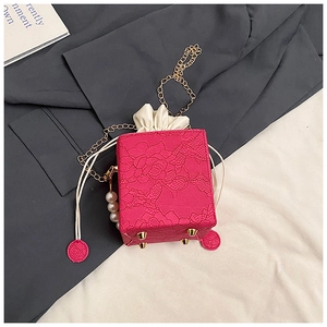 Detail of rose red lace mini bag with pearl charm and golden chain strap on fabric