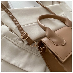 Detail of tan faux leather crossbody bag with gold hardware and curved handle