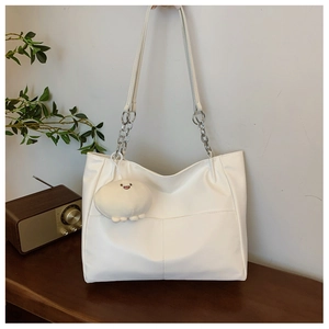 Detailed view of white tote bag with silver chain straps and plush charm in home setting