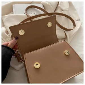 Detail view of the brown leather crossbody bag showing dual magnetic buckles and interior