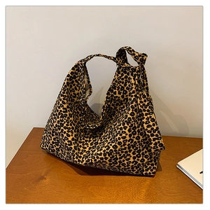 Detail of leopard print hobo bag with knotted handle and canvas texture on wood surface