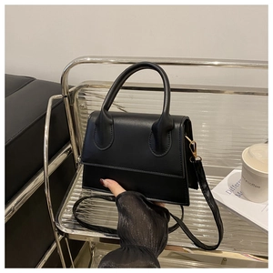 Detail of minimalist black crossbody bag with gold hardware and top handle on a chair