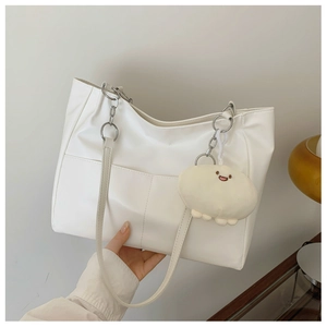 Detail of white leather tote bag featuring metal chain strap and plush smiley charm