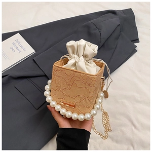 Detail of square lace bucket bag with pearl handle and gold chain on gray fabric