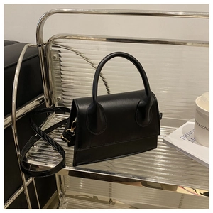 Detail of black matte leather handbag with gold hardware and round handle on a modern shelf