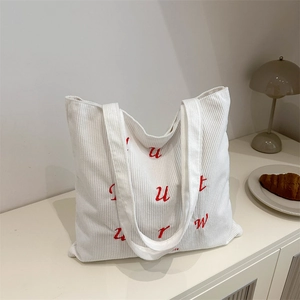 White corduroy tote bag with red embroidered letters shown in a cozy home setting