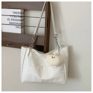 Detail of white leather tote with silver chain strap and cute plush charm on wood stand
