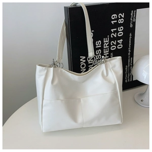 Detail of white tote bag featuring two front pockets and silver metal hardware accents