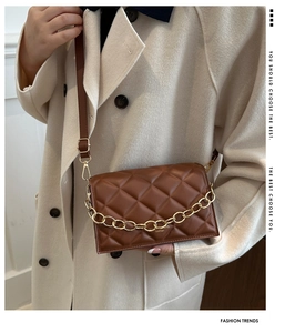 Brown quilted crossbody bag with gold chain detail worn over a white coat