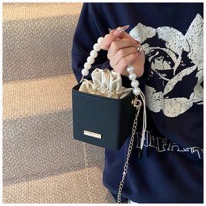 Detail of black embossed square bucket bag with pearl handle and golden chain strap