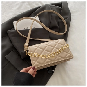 Close-up of beige quilted crossbody bag with gold chain on a grey blazer and white sheets